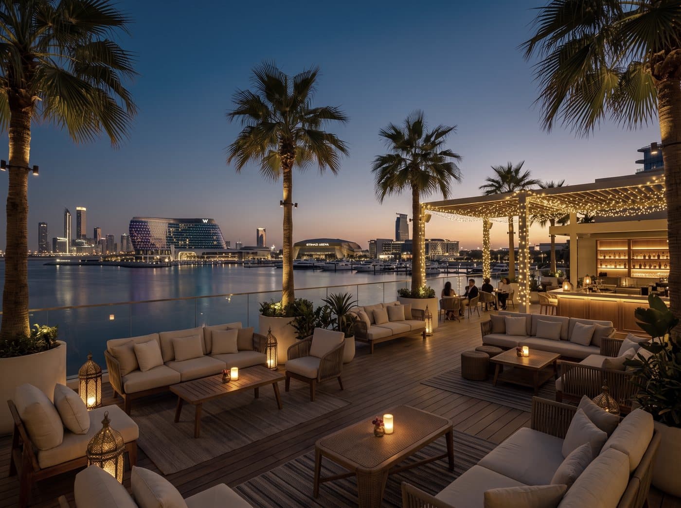 Symbolbild: eine Lounge-Terrasse am Wasser zur blauen Stunde, mit Laternen, Palmen und Blick auf die Skyline
