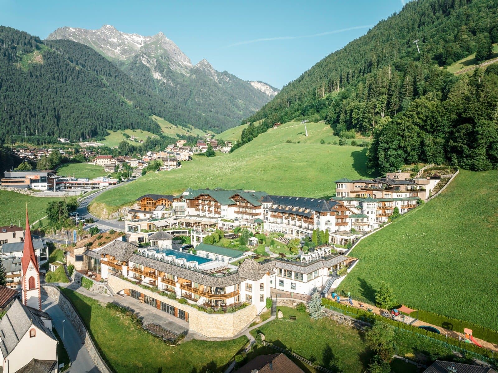 Luftaufnahme des STOCK Resort in Finkenberg mit Kirche und Bergwiesen