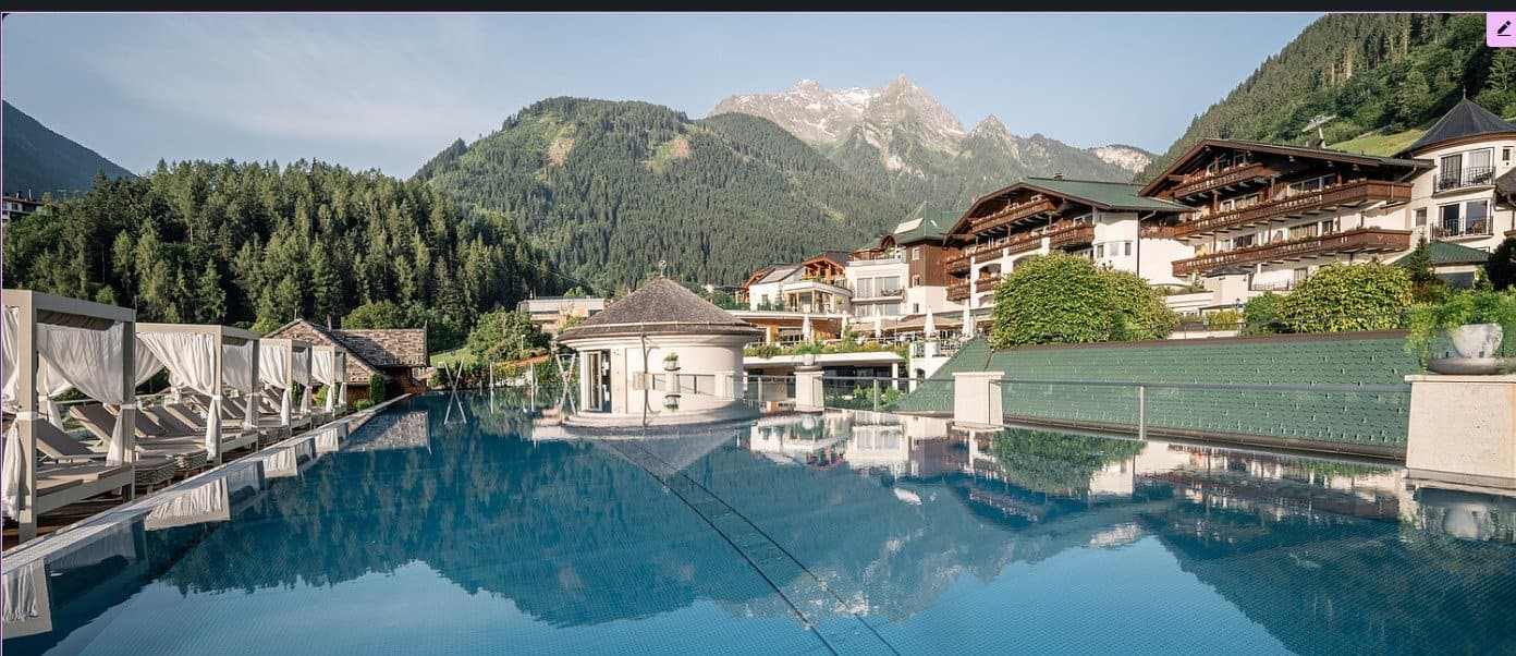 Infinity-Pool des STOCK Resort, in dem sich Hotel und Berge spiegeln