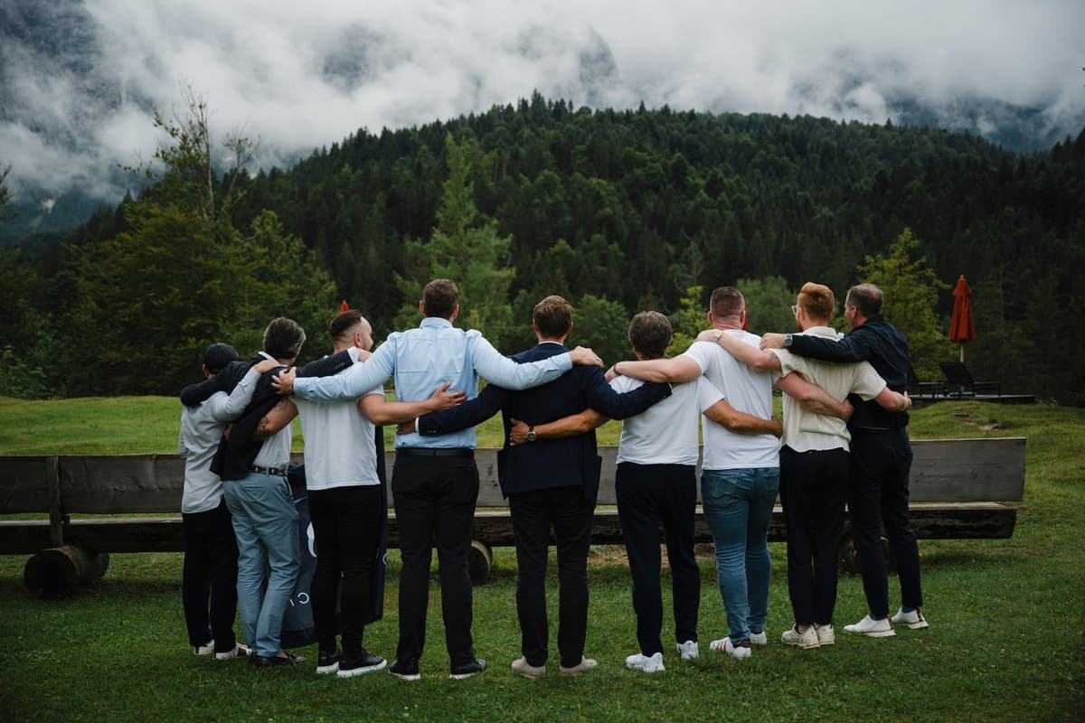 Mitglieder der Unicorn Society stehen Arm in Arm auf einer Wiese vor bewaldeten Bergen