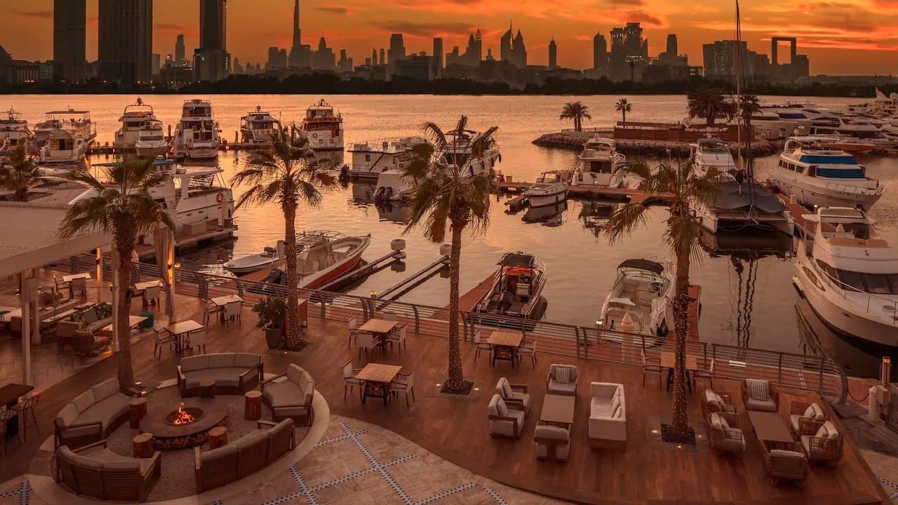 Terrasse mit Feuerstelle am Yachthafen bei Sonnenuntergang, dahinter die Skyline von Dubai