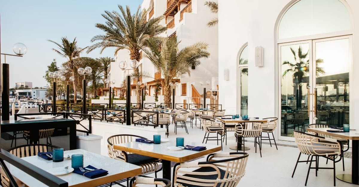 Gedeckte Restaurantterrasse zwischen Palmen und weißen Fassaden